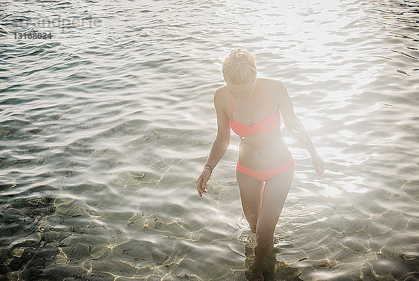 Mittelgroße erwachsene Frau im Bikini  die im sonnenbeschienenen Meer paddelt