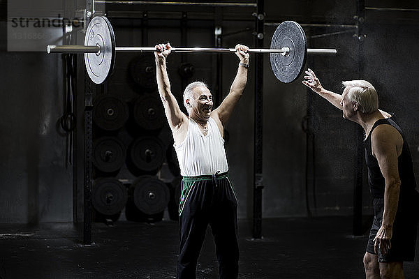 Ältere Männer trainieren mit Langhantel in dunkler Turnhalle