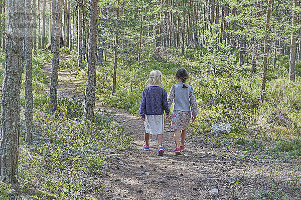 Rückansicht von zwei Mädchen in Retro-Kleidung beim Waldspaziergang