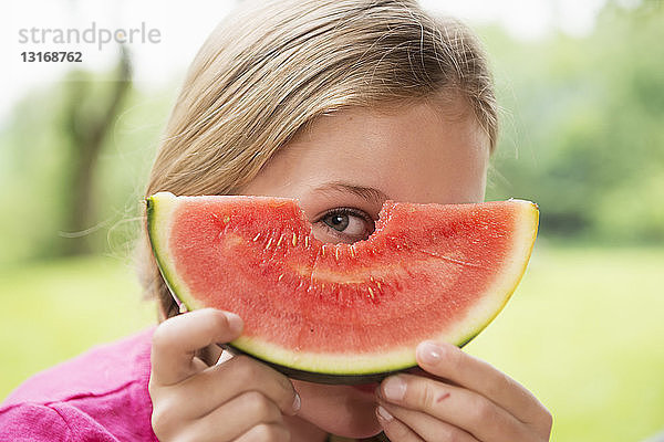 Nahaufnahme eines Mädchens  das durch eine Wassermelonenscheibe schaut