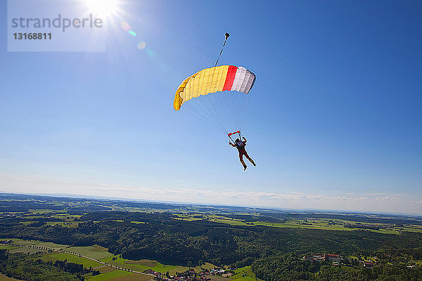 Mann springt mit dem Fallschirm über ländlicher Landschaft ab