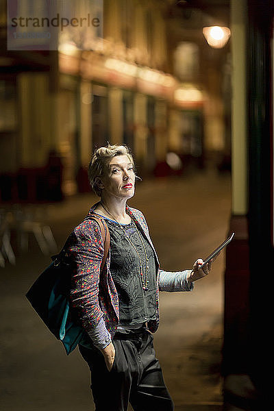 Portrait einer reifen Frau  die nachts auf der Straße ein digitales Tablet benutzt  London  UK