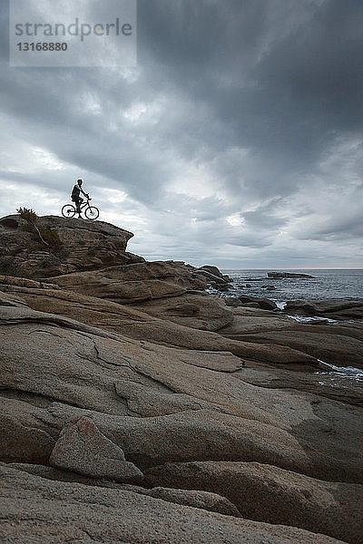 Mann sitzt auf Fahrrad auf Felsbrocken