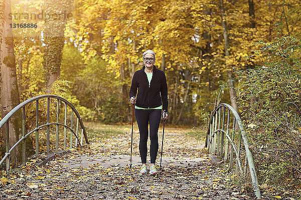 Senioren-Nordic-Walkerin überquert Fußgängerbrücke im Herbstpark