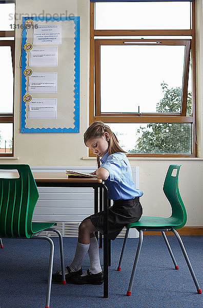 Schulmädchen liest ein Buch am Schreibtisch in einem Klassenzimmer