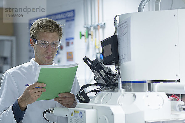 Männlicher Wissenschaftler liest Notizbuch im Labor