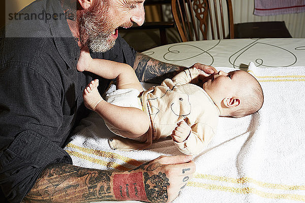 Vater unterhält Baby-Sohn auf Wohnzimmertisch liegend