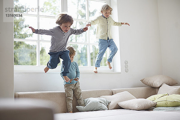 Drei Jungen springen vom Fensterbrett auf das Sofa  mittlere Luft