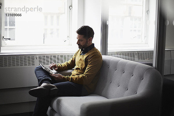 Lässiger Geschäftsmann auf Sofa sitzend mit digitalem Tablet