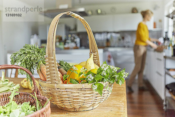 Gartenprodukte  in Körben auf dem Tisch in der Küche  reife Frau arbeitet im Hintergrund