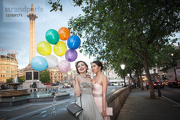 Zwei junge Freundinnen in Abendkleidern posieren mit Luftballons  Trafalgar Square  London  UK