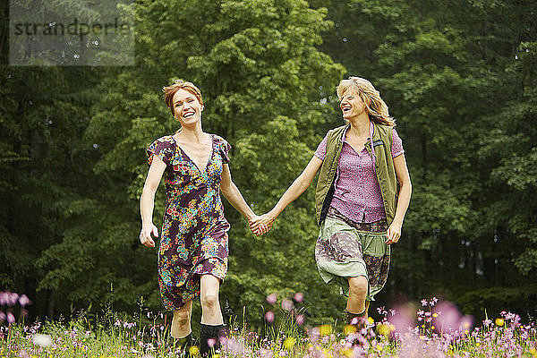 Zwei Frauen halten sich an den Händen und rennen auf einer Wildblumenwiese