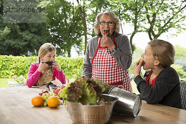 Zwei Schwestern und eine Großmutter essen auf der Terrasse frisches Obst