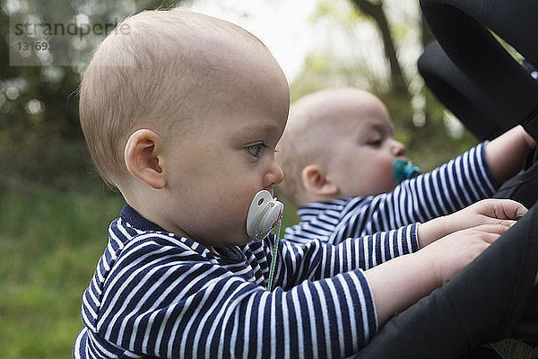 Kleine Zwillingsbrüder mit Schnullern  die mit ihren Kinderwagen spielen