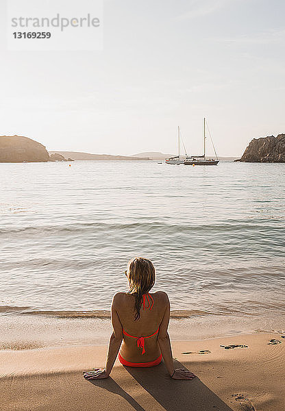 Rückansicht einer Frau  die vom Strand aus nach außen schaut  Menorca  Balearen  Spanien