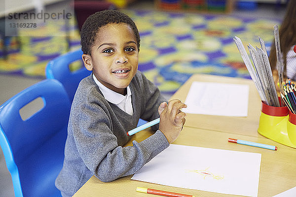 Porträt eines Jungen  der am Schreibtisch im Klassenzimmer der Grundschule zeichnet