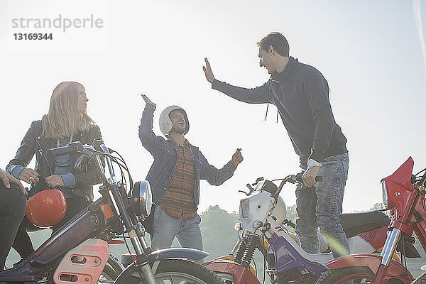 Gruppe von Freunden sitzt auf einem Moped  zwei Männer geben High Five