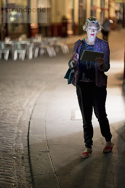 Reife Frau benutzt nachts auf der Straße ein digitales Tablet  London  UK