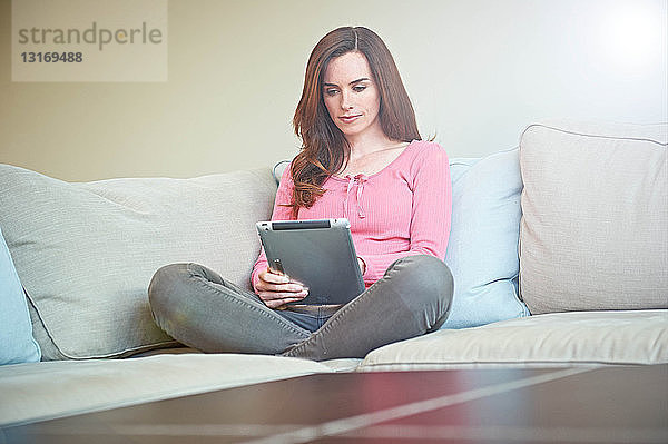 Frau benutzt digitales Tablett auf dem Sofa