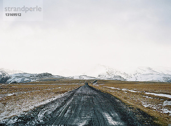 Schotterpiste und entfernte schneebedeckte Berge  Island