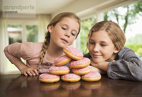 Zwei Schwestern starren auf einen Stapel mit Donut-Löchern auf der Küchentheke