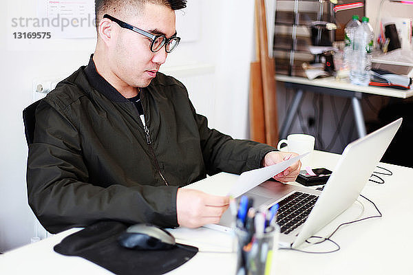 Männlicher Architekt liest am Büroschreibtisch Papierkram