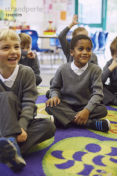 Kinder sitzen im Schneidersitz auf dem Boden im Klassenzimmer der Grundschule