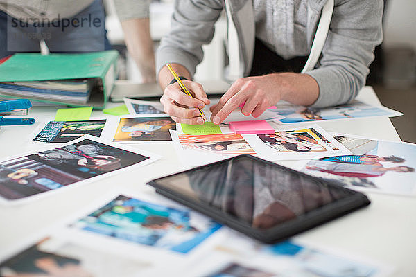 Junger Mann macht Notizen auf dem Schreibtisch von Fotos mit digitalem Tablett im Kreativbüro