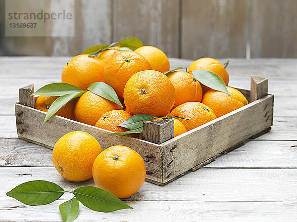 Orangen in alter Kiste auf gekalktem Holztisch