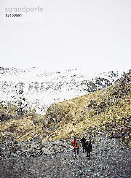 Rückansicht von drei Touristen  die auf schneebedeckte Berge zulaufen  Island