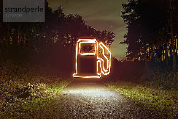 Leuchtendes Zapfsäulensymbol über der Forststraße bei Nacht