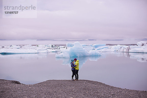 Seitenansicht eines mittelgroßen erwachsenen Paares  von Angesicht zu Angesicht umarmt am Gletschersee Jokulsarlon  Island
