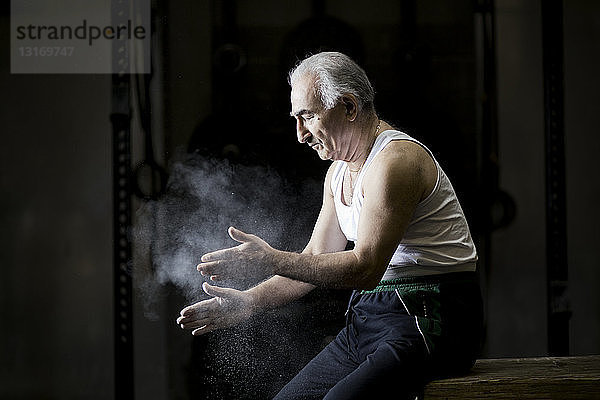 Älterer Mann sitzt kreidebleich an den Händen in dunkler Turnhalle