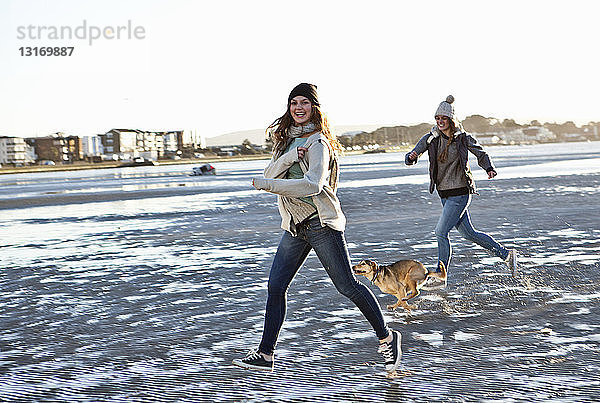 Zwei Freundinnen laufen mit Hund am Strand