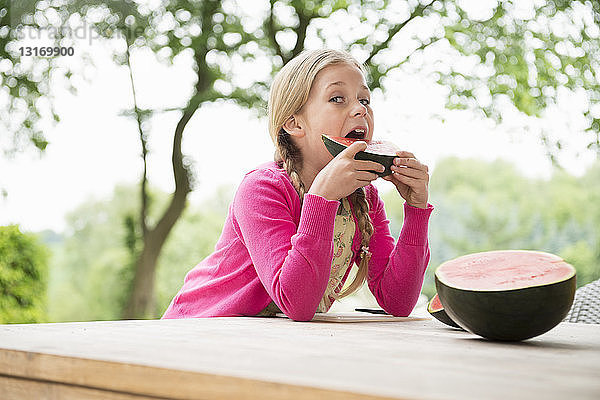 Mädchen am Terrassentisch beim Essen einer Wassermelonenscheibe