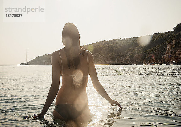 Rückansicht einer jungen Frau im Bikini  die im Meer watend  Menorca  Balearen  Spanien