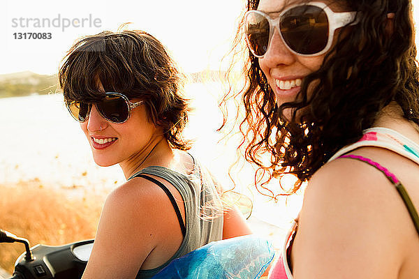 Lächelnde Frauen fahren Roller am Strand