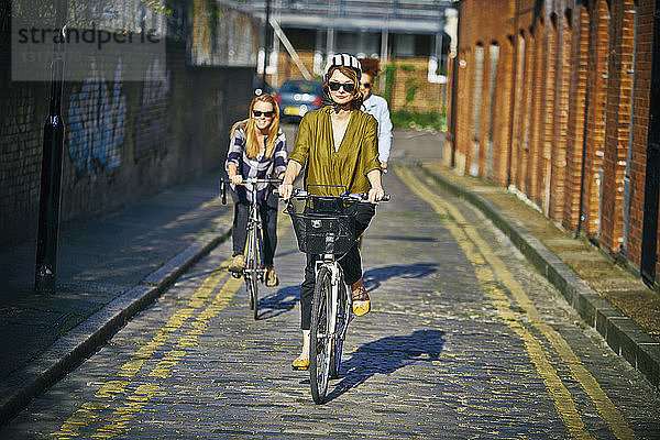 Frontansicht von Frauen mit Sonnenbrille beim Fahrradfahren auf Kopfsteinpflaster