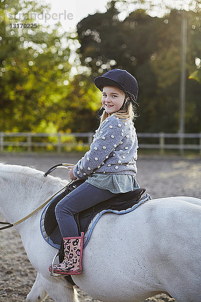 Porträt eines glücklichen Mädchens auf weissem Pony auf einem Reitplatz