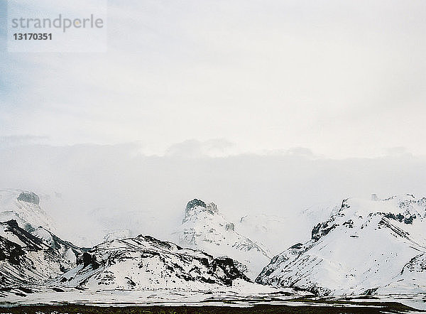 Blick auf schneebedeckte Berge und niedrige Wolken  Island