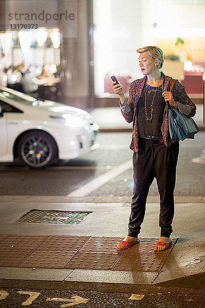Reife Frau  die nachts auf der Straße mit einem Smartphone simst  London  UK