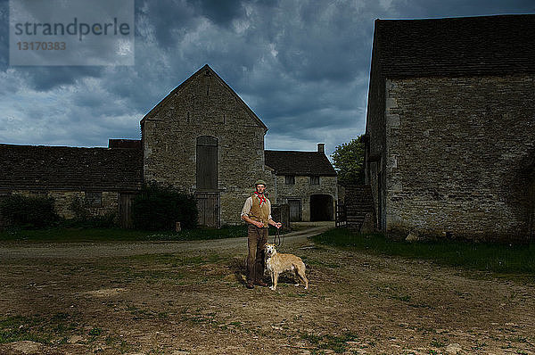 Porträt eines reifen traditionellen Bauern und seines taumelnden Hundes auf dem Bauernhof