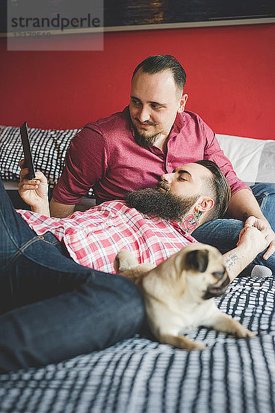 Homosexuelles Paar mit Hund  benutzt Smartphone im Schlafzimmer