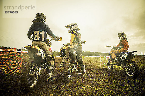 Junge Männer und Jungen auf Motorrädern beim Motocross