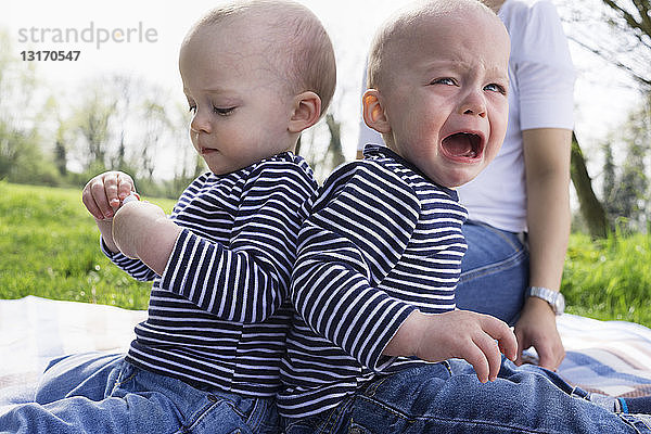 Kleine Zwillingsbrüder Rücken an Rücken auf einer Picknickdecke im Feld