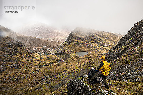 Wanderer steht auf einem Felsvorsprung des Bla Bheinn-Berges und trotzt den nassen und windigen Elementen der schottischen Highlands im Frühling  Isle of Skye  Schottland
