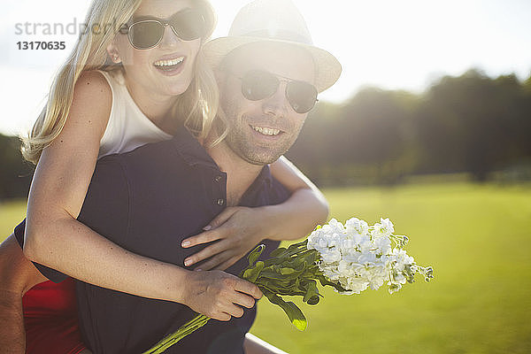 Junge Frau mit Blumen  die im Park von ihrem Freund Huckepack genommen wird