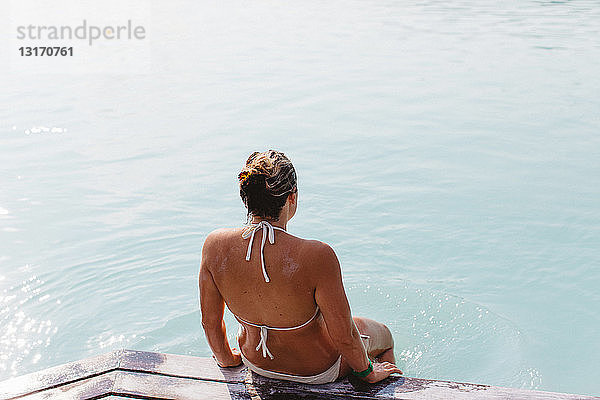 Hochwinkel-Rückansicht einer mittelgroßen erwachsenen Frau im Bikini am Pier sitzend  Blue Lagoon hot springs  Island