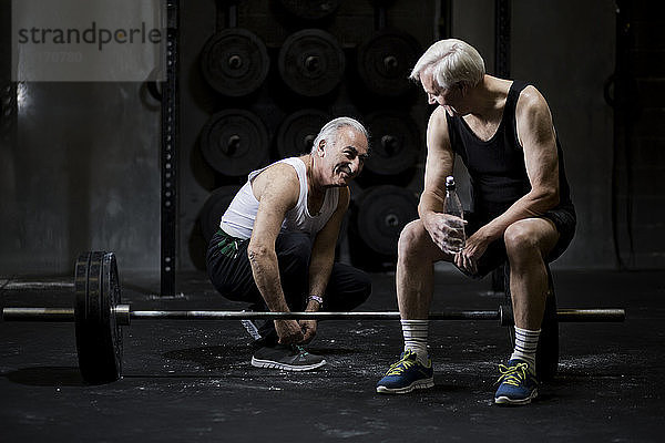 Ältere Männer plaudern und schnüren Trainerschnürsenkel in dunkler Turnhalle