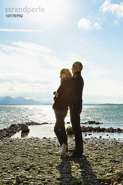 Ein erwachsenes Paar steht am See  umarmt sich  schaut auf die Aussicht